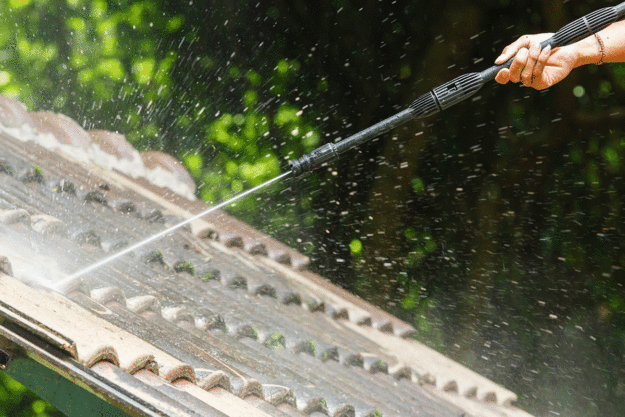 close up of man pressure washing house roof | pros and cons of DIY pressure washing