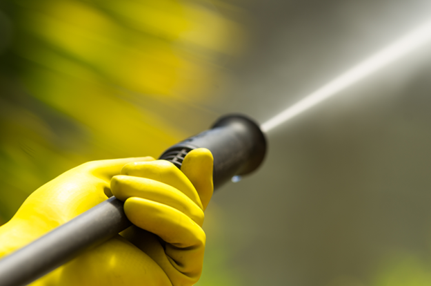 close up of pressure washer held by hand wearing yellow rubber gloves | pressure washing prices