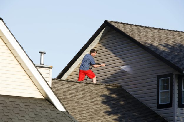 man on the roof of a house pressure washing siding | clean oxidized vinyl siding