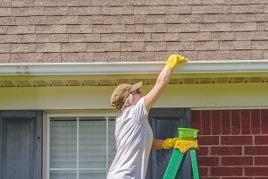 Woman Cleaning Gutters While Standing On Ladder | preparing your home for pressure washing