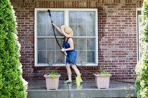 woman standing on a patio washing the windows of her house | pressure wash house before painting