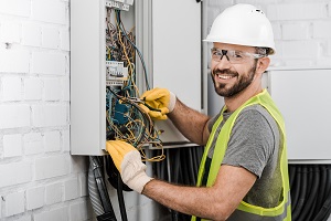 smling electrician repairing electrical box with pliers in corridor | building maintenance