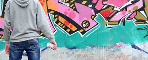 graffiti artist in a gray hoodie looks at the wall with his graffiti in pink and green colors on a wall | maintain commercial shopping center