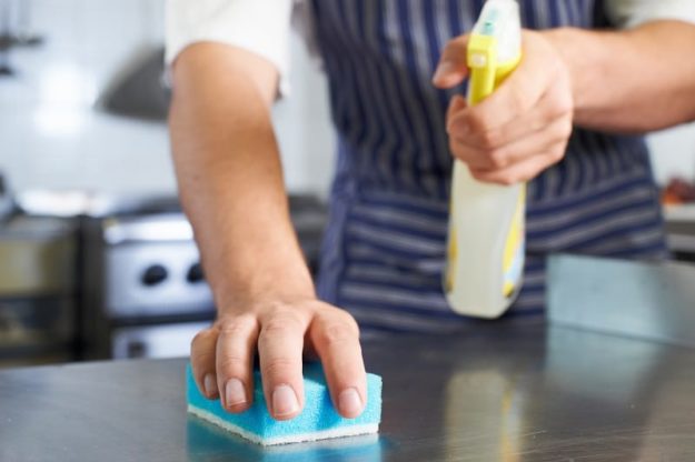worker at a restaurant cleaning kitchen with sponge and detergent spray | restaurant cleaning checklist